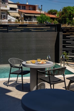 Uma área de refeições à beira da piscina, com uma mesa redonda, duas cadeiras e um pequeno balcão.