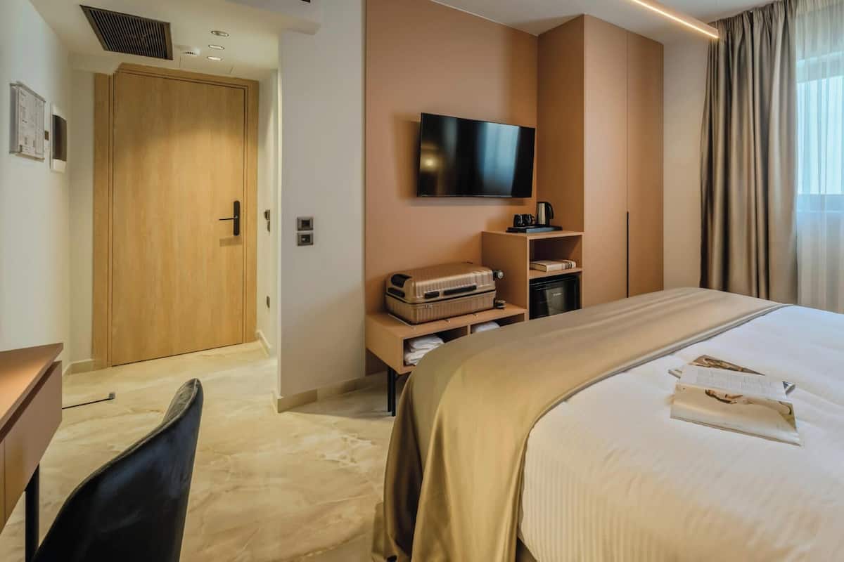 A hotel room with a bed, a TV mounted on the wall, a desk, and a chair.