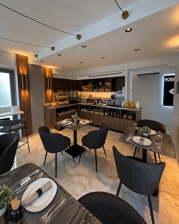 A modern dining area with tables set for four, a kitchen with a buffet, and a sign reading 'NOMA'.. Noma Smart Property by Airstay