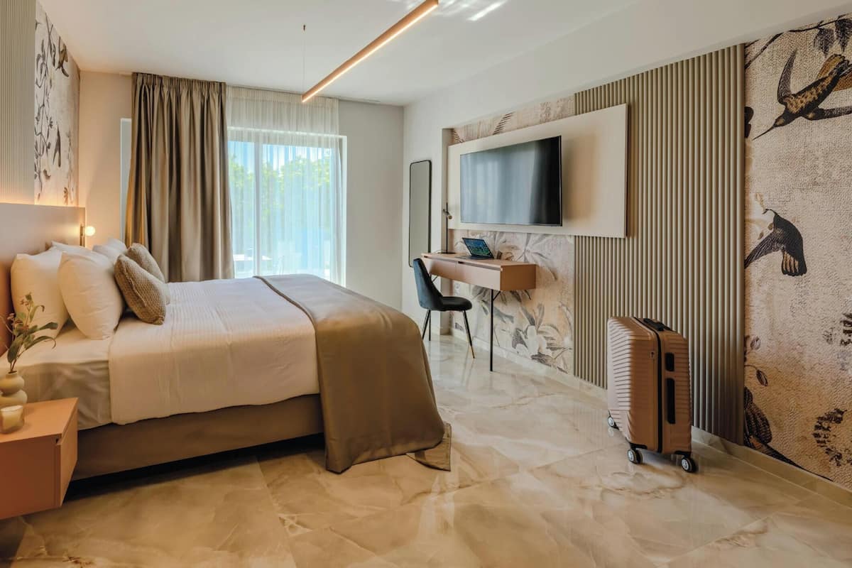 A modern hotel room with a bed, desk, TV, and a wall with a bird pattern.