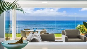 Un salon moderne avec vue sur l’océan, un coin repas et une grande plante.