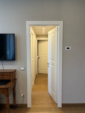 A hallway with a wooden floor, a television mounted on the wall, and a door leading to another room. - The Wisteria - Urban Oasis (Milan)