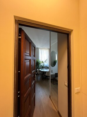 A hallway leading to a dining area with a table and chairs, a wooden door, and a mirror on the wall. - The Wisteria - Urban Oasis (Milan)