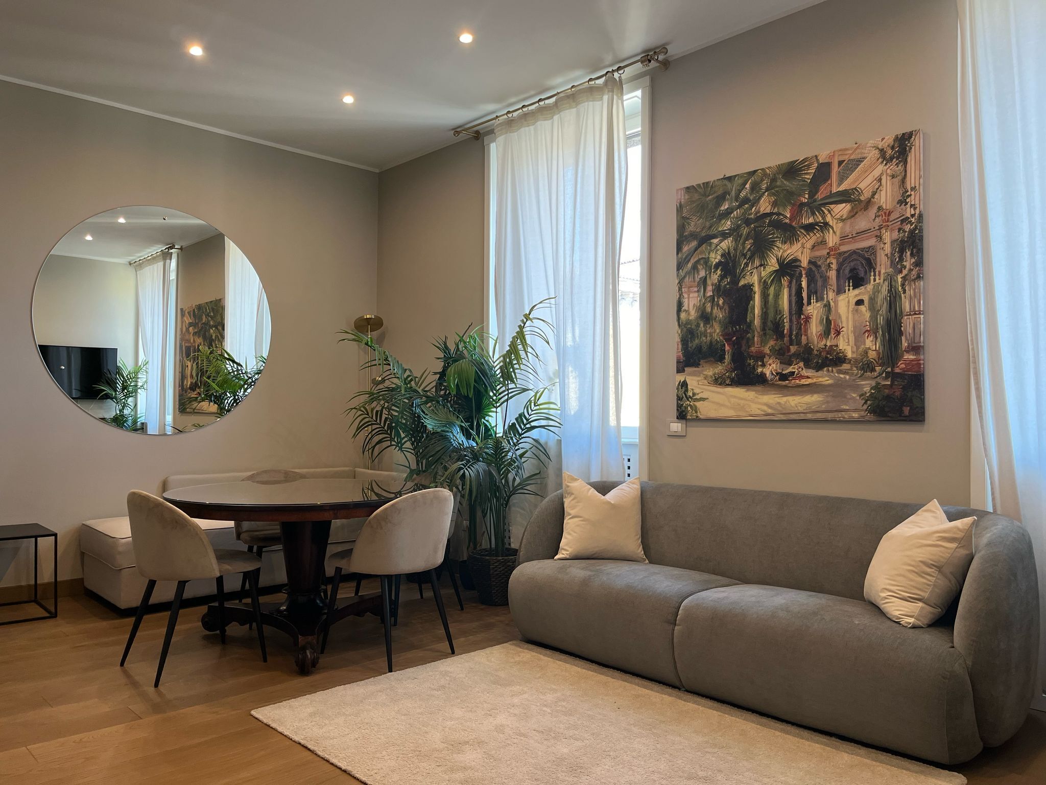 Ein Wohnzimmer mit einer Couch, einem Esstisch mit Stühlen, einem großen Spiegel, einer Zimmerpflanze und einem Gemälde an der Wand.