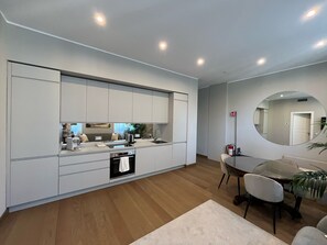 A modern kitchen with integrated appliances, a dining area with a round table and chairs, and a large mirror on the wall. - The Wisteria - Urban Oasis (Milan)