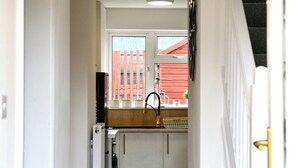 Un couloir menant à une cuisine avec une fenêtre, une porte et un escalier.