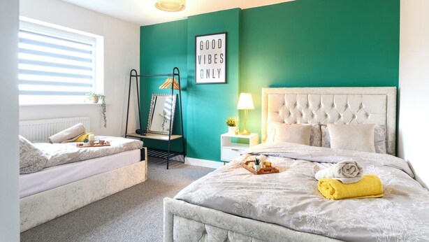 Une chambre avec un lit, une banquette, une étagère fixée au mur, une table de chevet, une lampe et un panneau indiquant « Seules les bonnes ondes sont les bienvenues ».