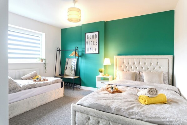 A bedroom with a bed, a daybed, a wall-mounted rack, a bedside table, a lamp, and a 'Good Vibes Only' sign. - Luxurious Retreat | Hot Tub | Man Cave | 9PPL (Whiston)