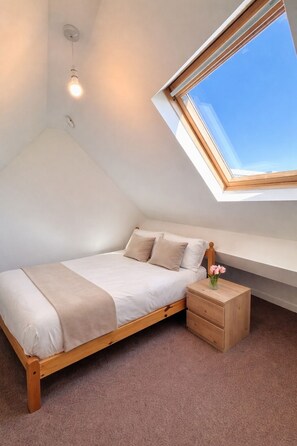 Una camera da letto con un soffitto a falde, un lucernario, un letto con struttura in legno, un comodino e un vaso con fiori.