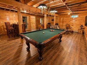 A wooden interior with a pool table, chairs, and a staircase.
