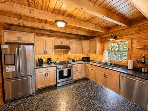 A kitchen with wooden cabinets, stainless steel appliances, granite countertops, and a window with a view of greenery.
