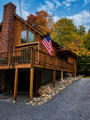 A wooden cabin with a balcony, an American flag, and a stone foundation.