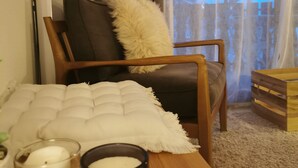 Un salon chaleureux avec un fauteuil en bois, un coussin blanc, une petite table avec des bougies et une vue sur un paysage enneigé par la fenêtre.
