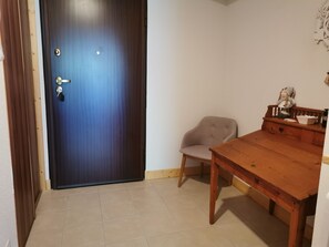 Ein Zimmer mit einem Holztisch, einem Stuhl, einer blauen Tür und einer kleinen Bank mit einer Figur.