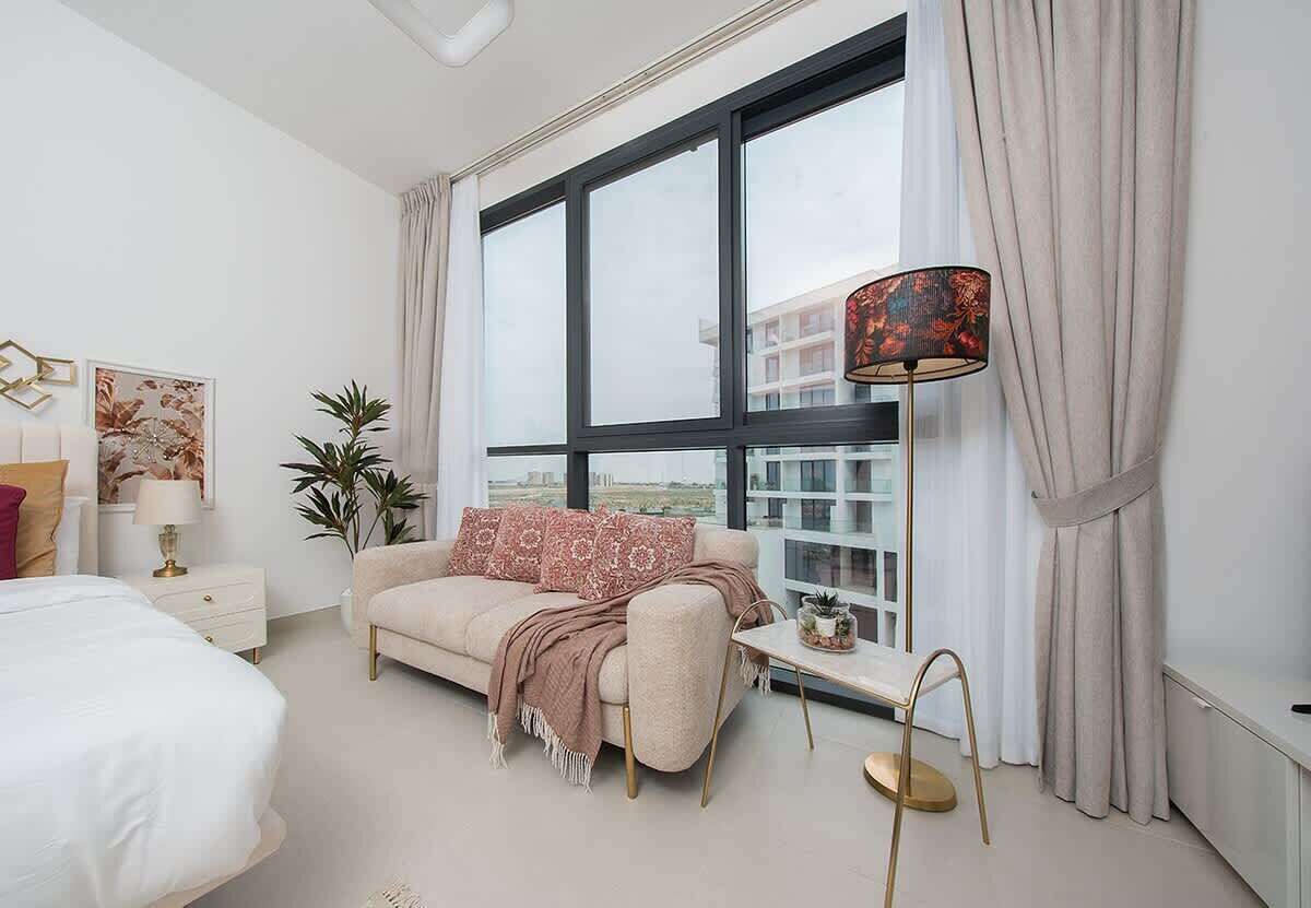 A modern bedroom with a large window, a sofa, a bedside table, and a lamp.