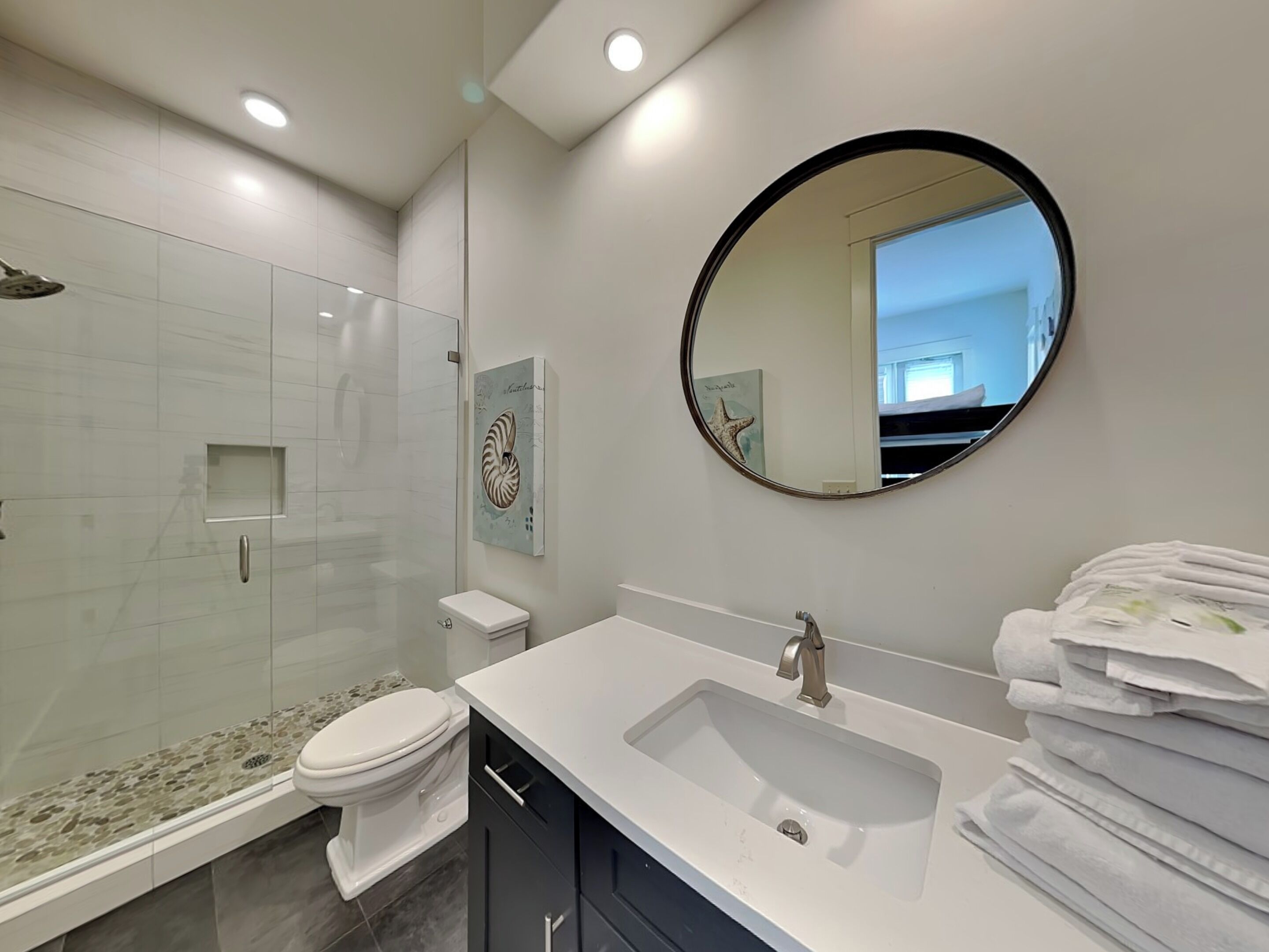 A modern bathroom with a glass shower enclosure, a white toilet, a sink with a mirror, and a towel rack.