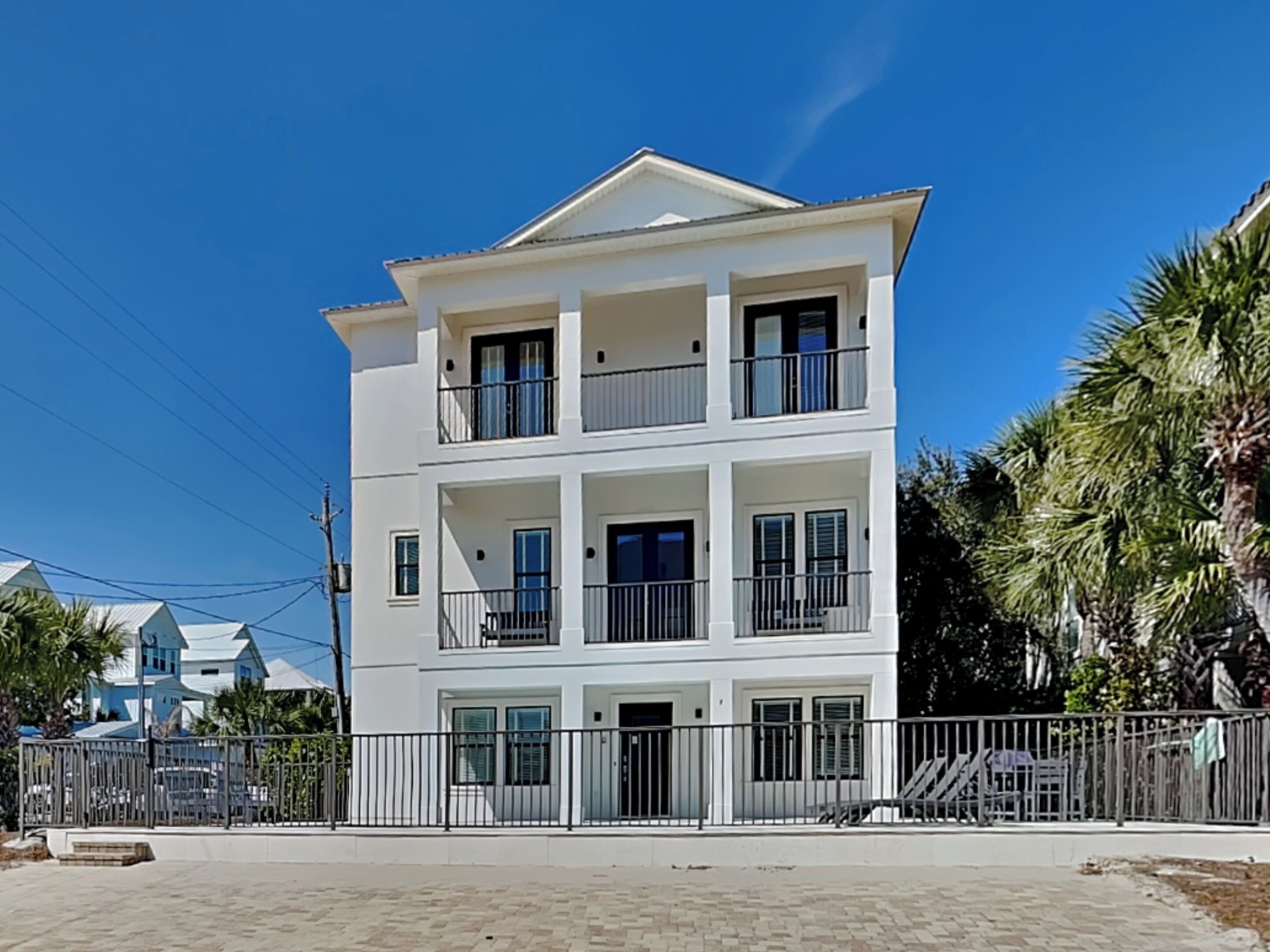 A multi-story white building with balconies, a gated entrance, and a paved area in front.