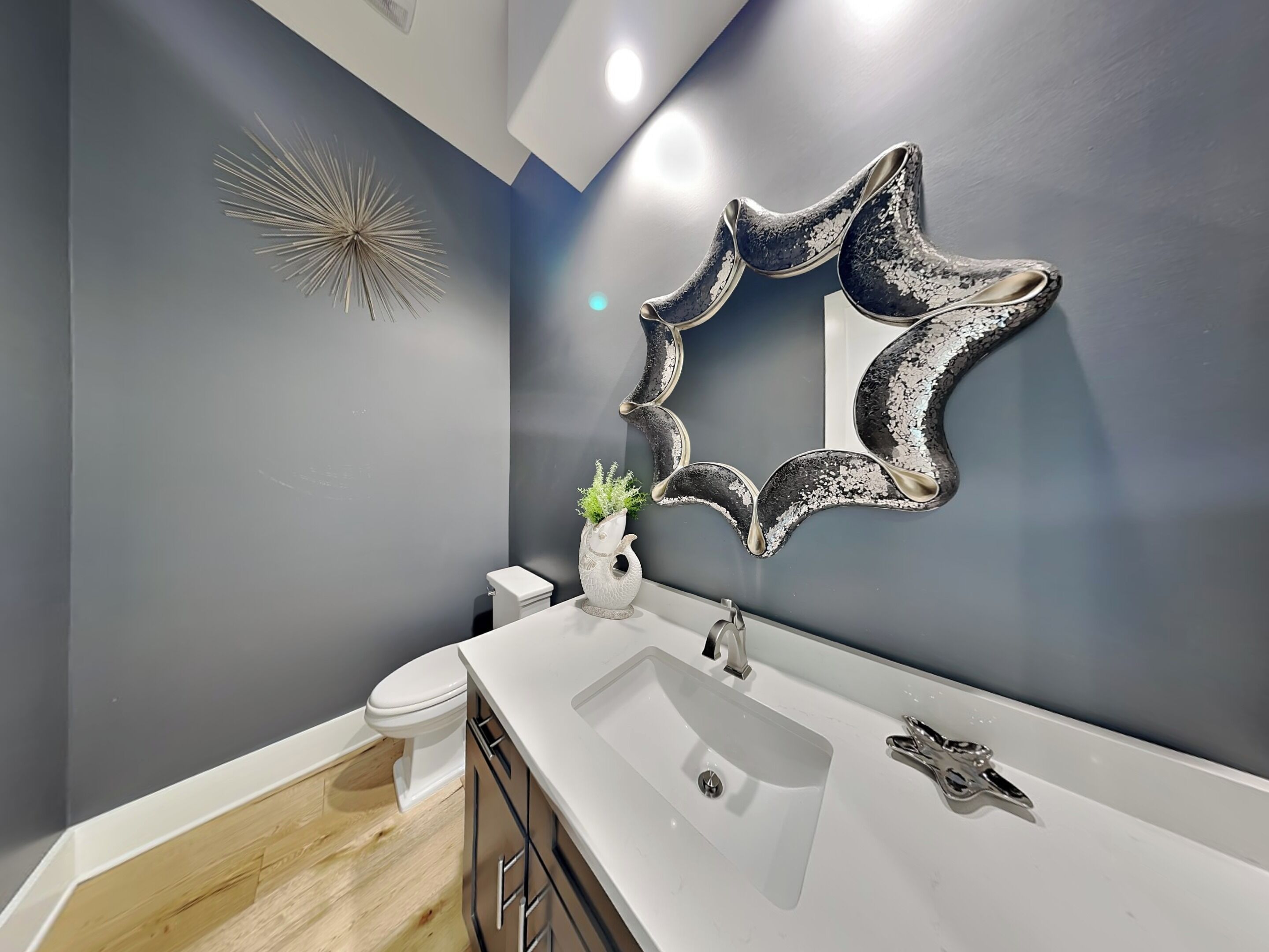 A modern bathroom with a white sink, a toilet, and a decorative mirror.