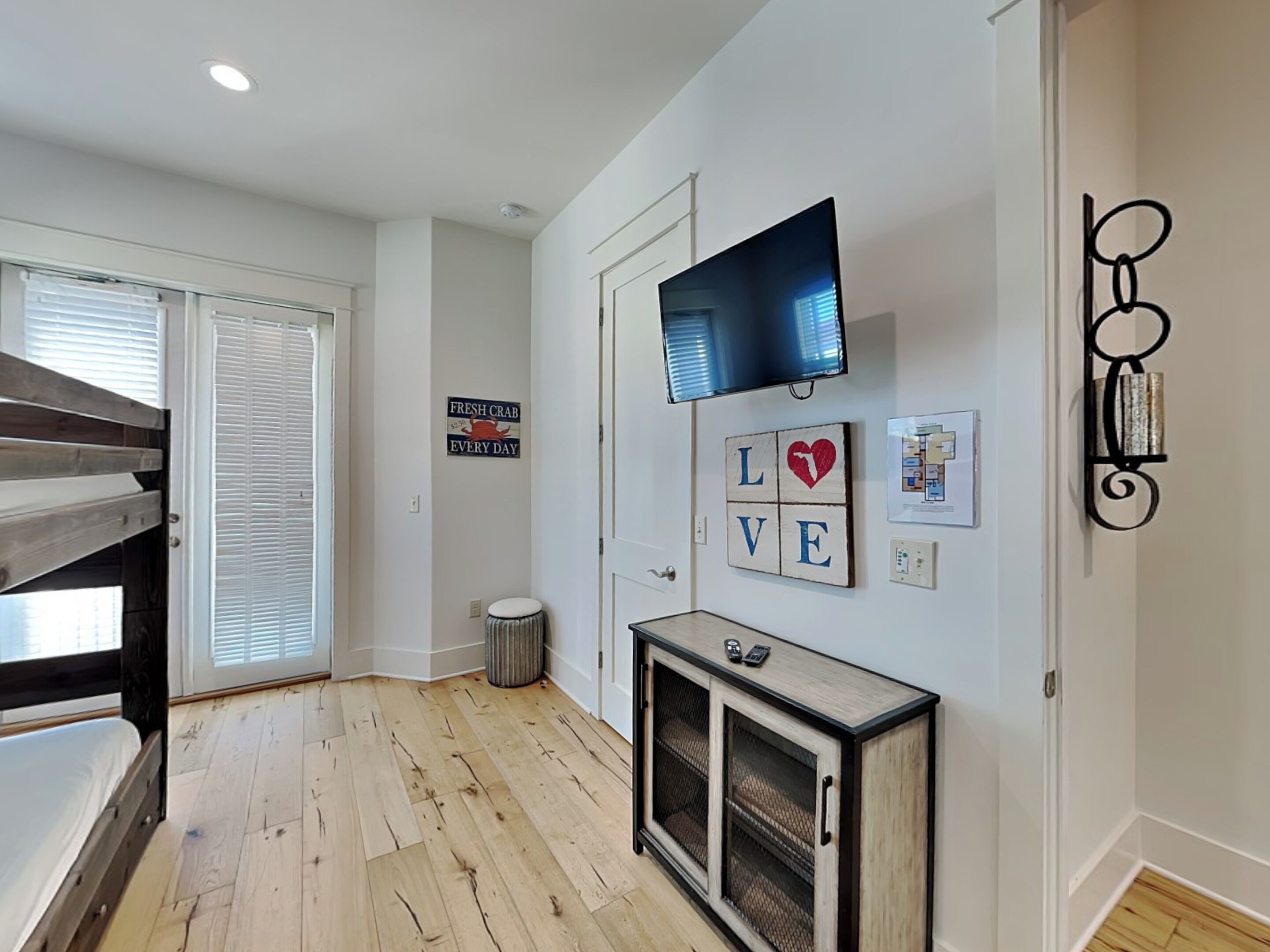 A modern interior with a wooden floor, a television mounted on the wall, a small cabinet, and a sign that reads 'FRESH CRAB EVERY DAY'.