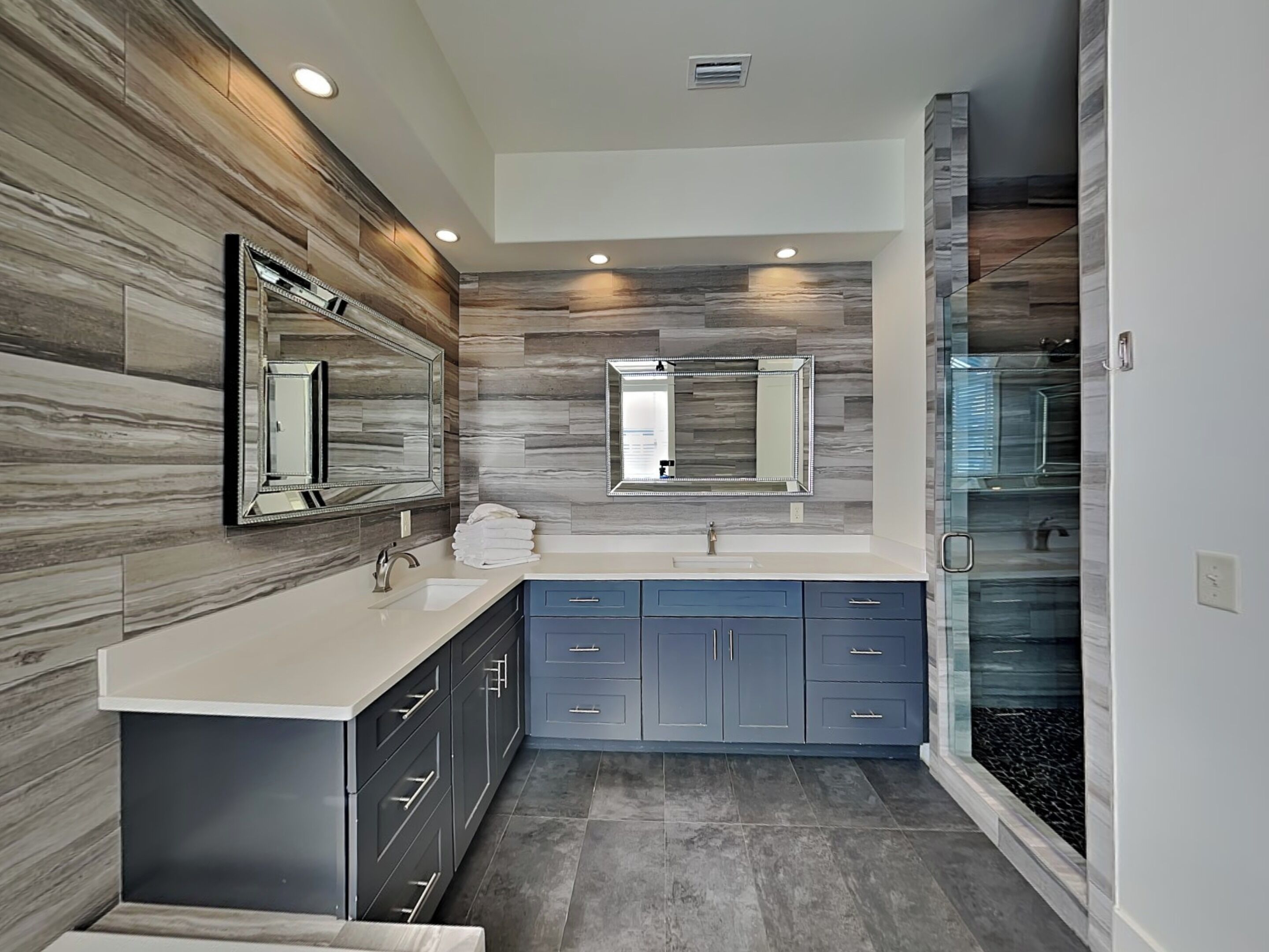 A modern bathroom with a marble backsplash, dual sinks, and a glass shower enclosure.