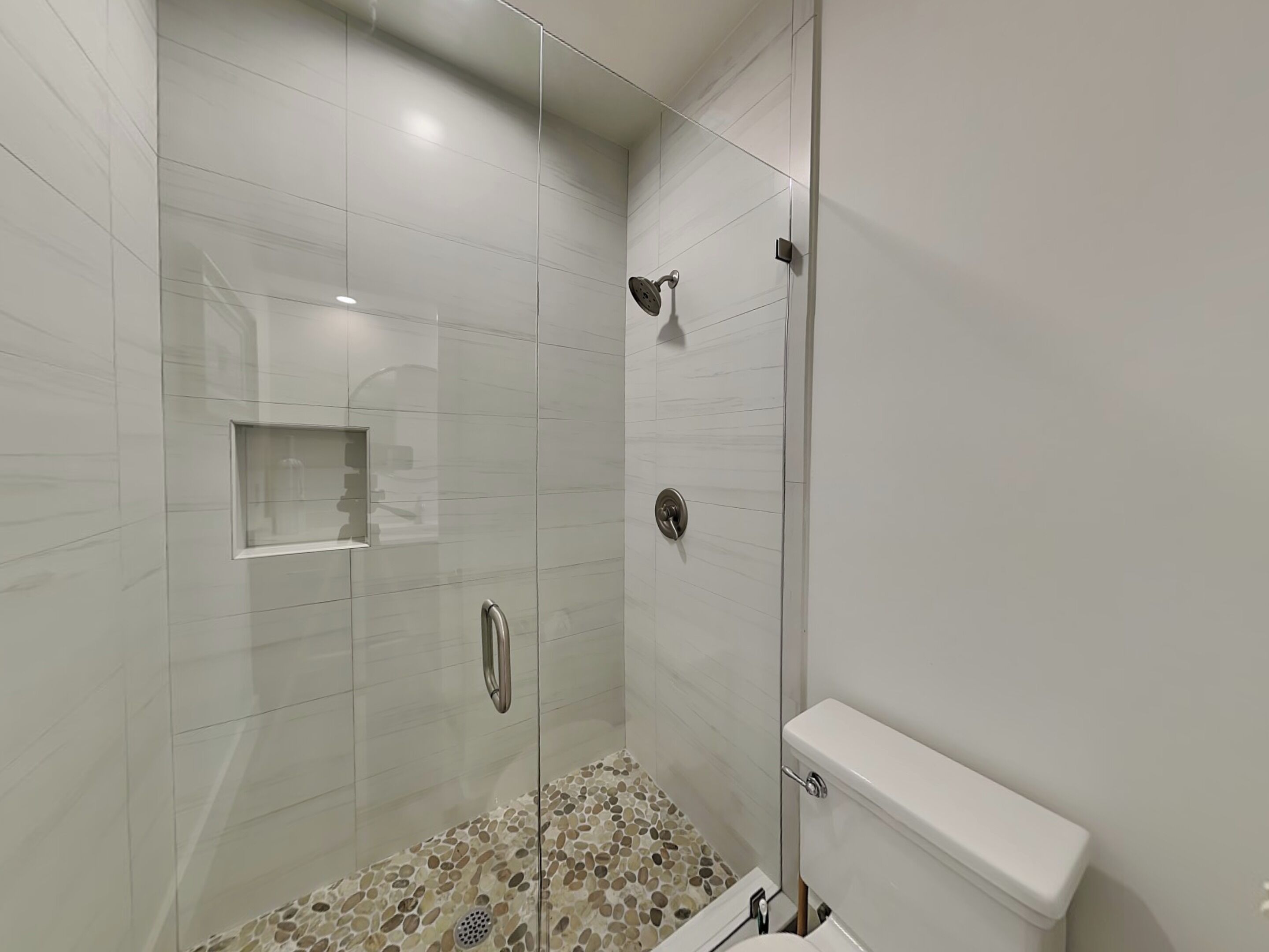 A modern bathroom with a glass-enclosed shower, a toilet, and a small shelf.
