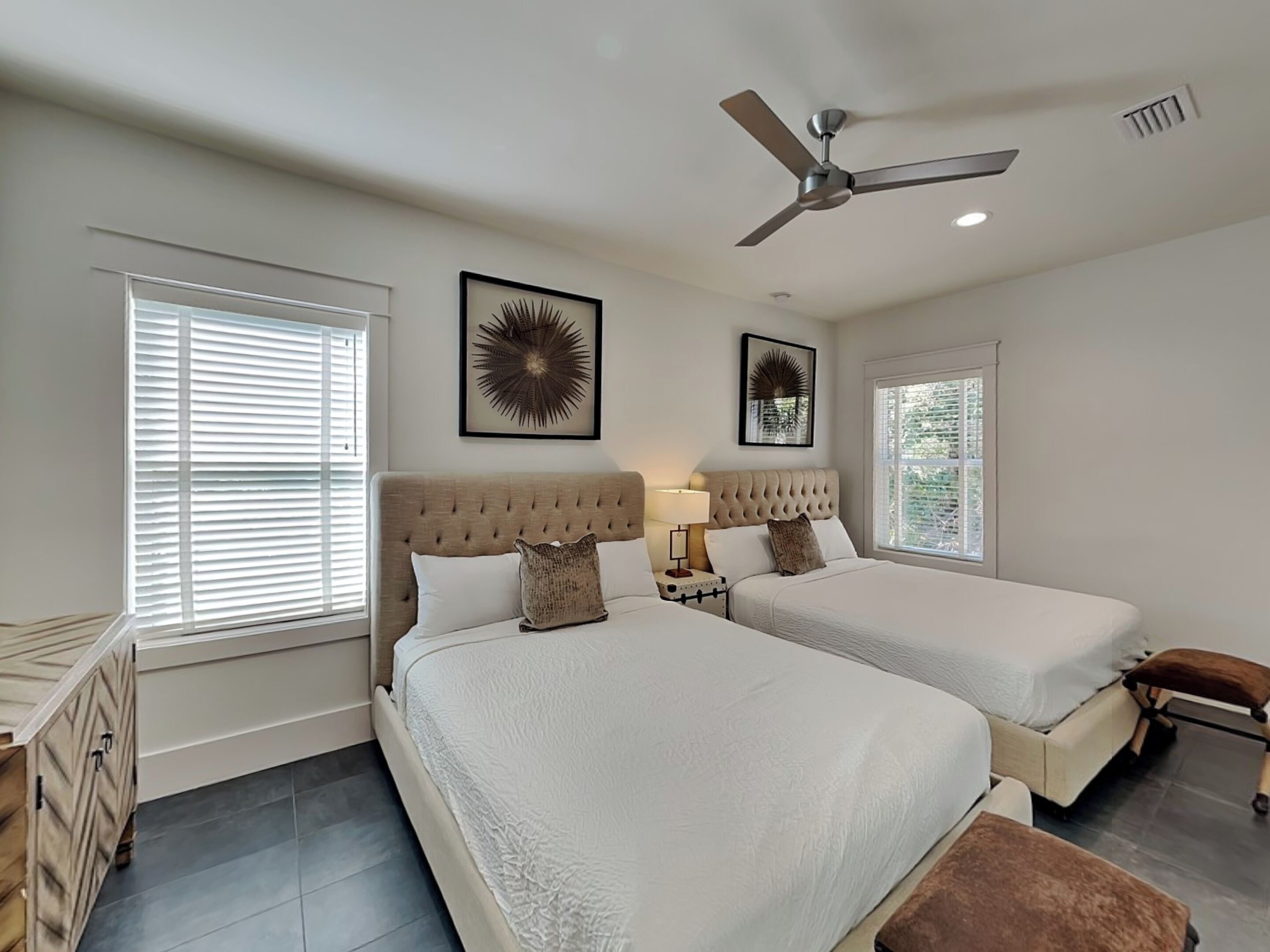 A bedroom with two beds, a ceiling fan, and a window with blinds.