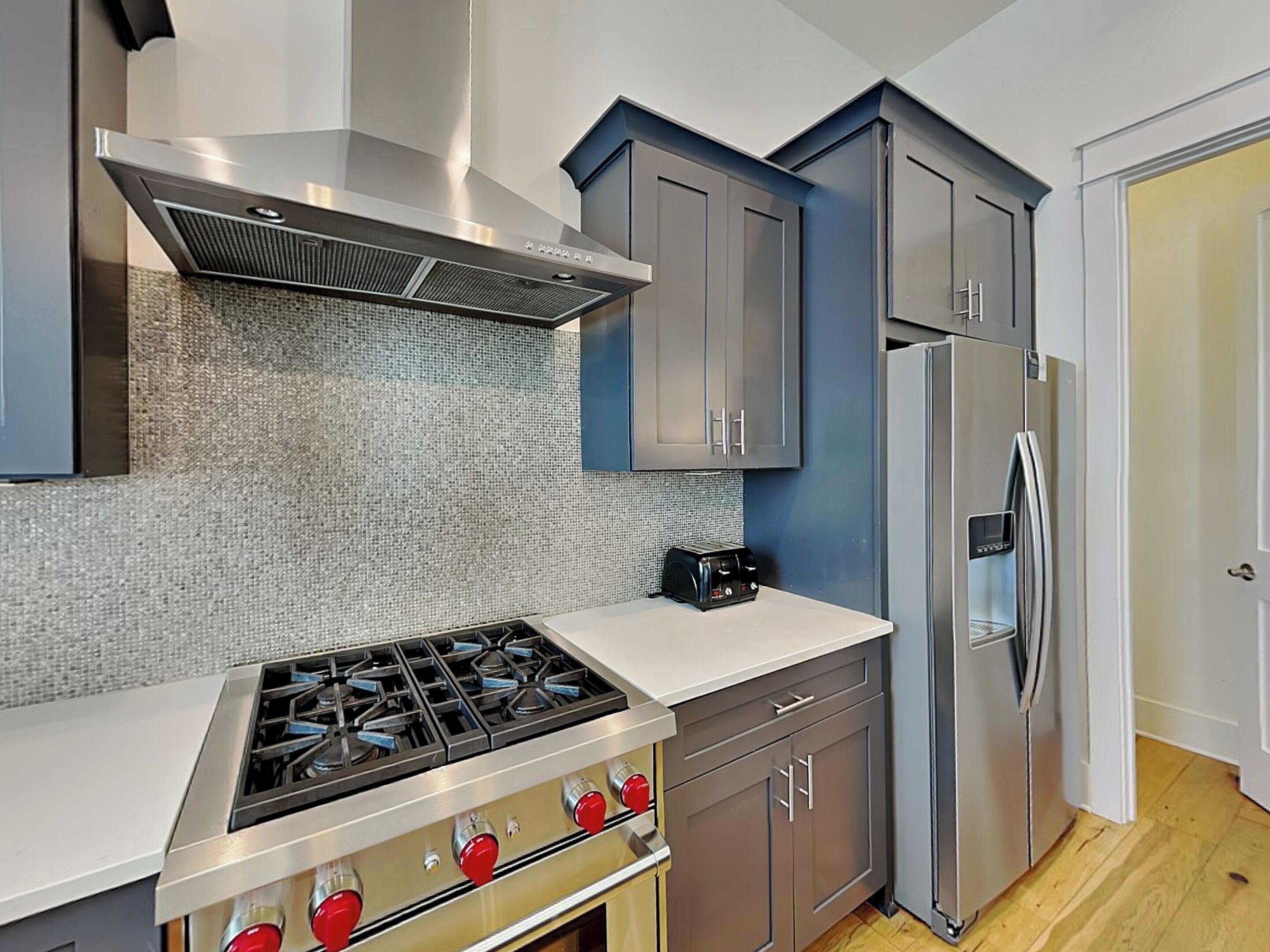 Une cuisine moderne équipée d’une cuisinière à gaz, d’appareils électroménagers en acier inoxydable et de meubles de rangement gris.