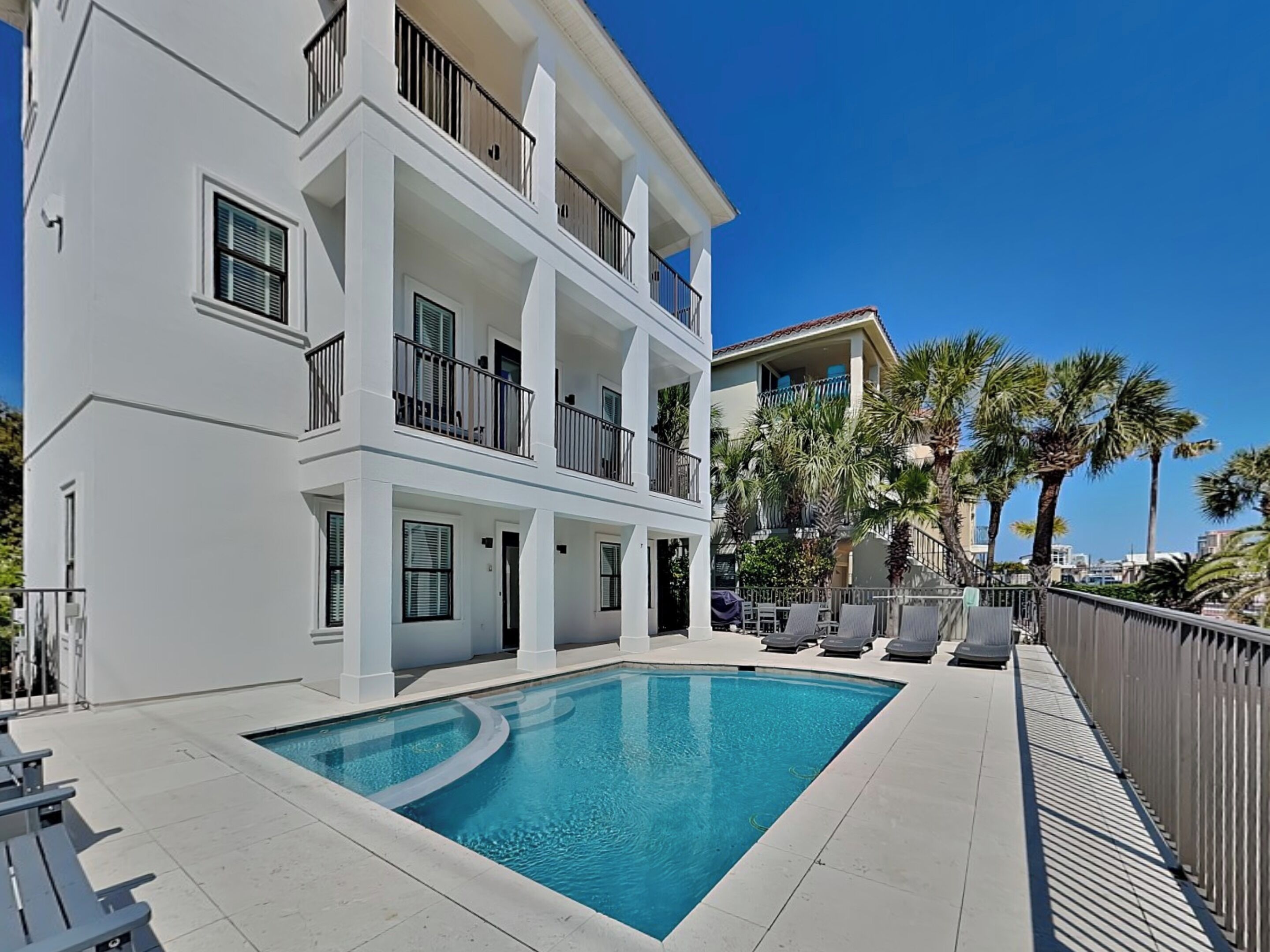 A multi-story hotel with a swimming pool, balconies, and palm trees.