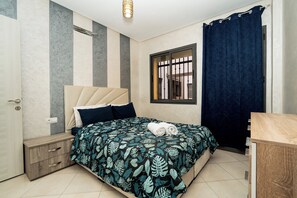Ein Schlafzimmer mit einem Bett, Nachttischen, einem Fenster mit Gitter und einem Vorhang.