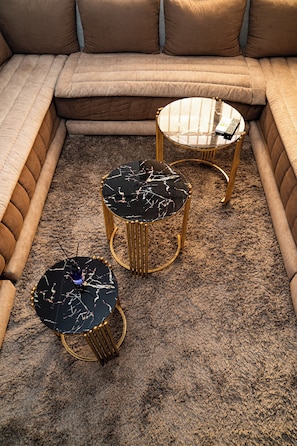 Ein modulares Sofa mit drei runden Beistelltischen, jeweils mit Marmorplatte und goldenen Beinen.