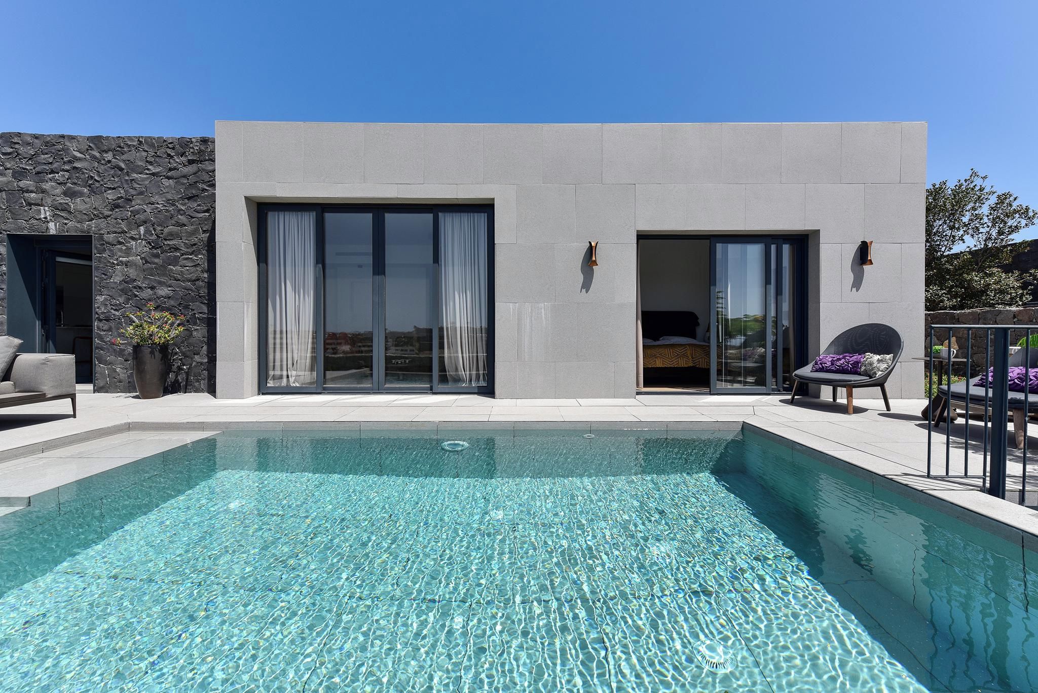 Un edificio moderno con piscina, puertas correderas de vidrio y mobiliario exterior.