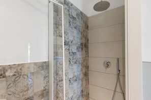 Un espace douche avec des carreaux décorés, une porte en verre et un pommeau de douche.