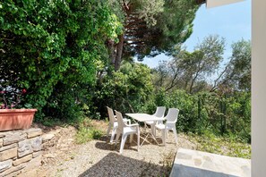 A patio with a table and chairs, surrounded by greenery and a stone wall.
