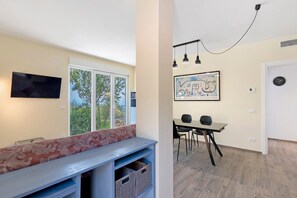 A modern room with a TV, a bench with a floral cushion, a dining area with a table and chairs, and artwork on the wall. - Villa 'Casablanca' with Sea View, Wi-Fi and Air Conditioning (Cipressa)