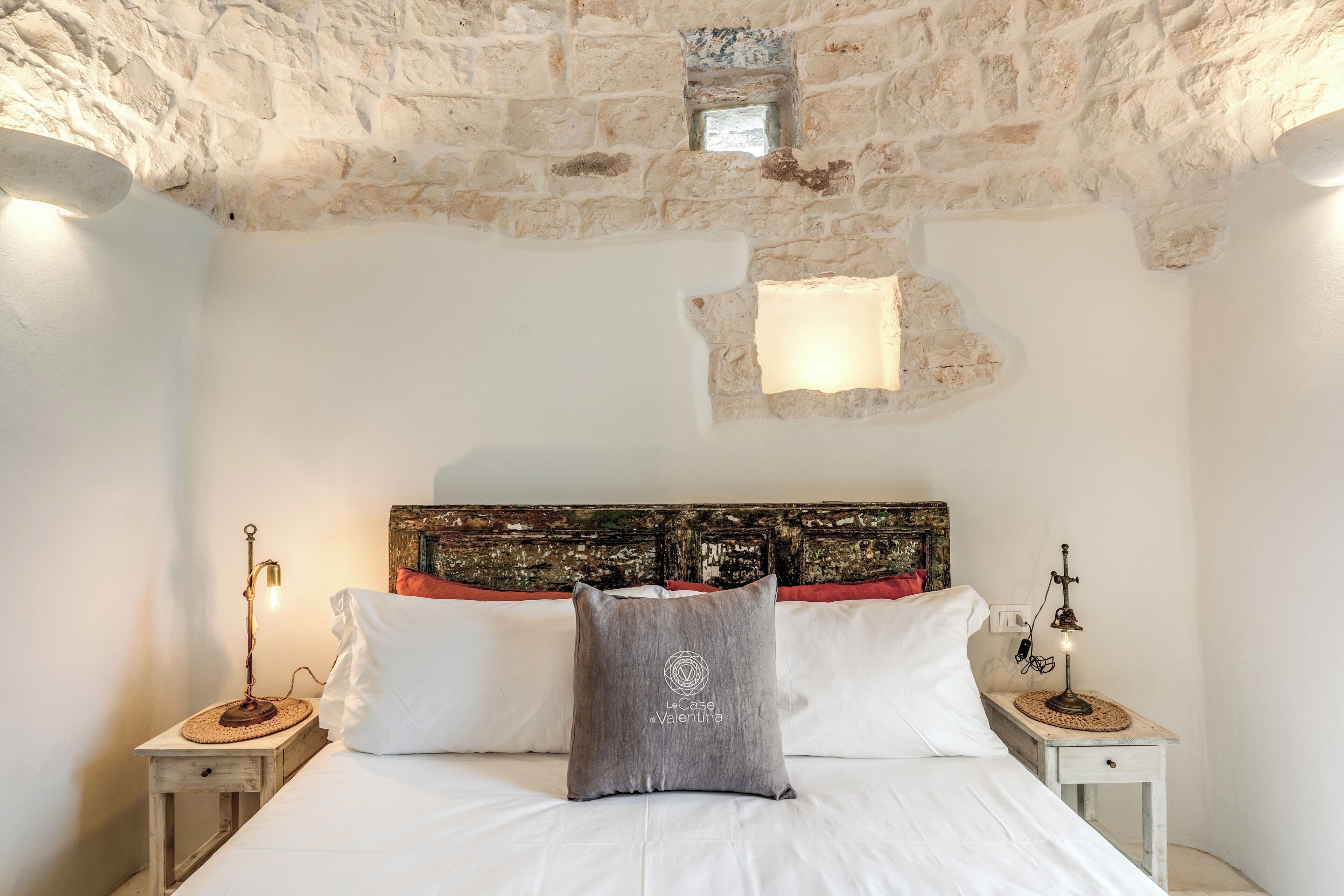 A bedroom with a stone ceiling, a bed with white linens, a decorative headboard, and two bedside tables with lamps.