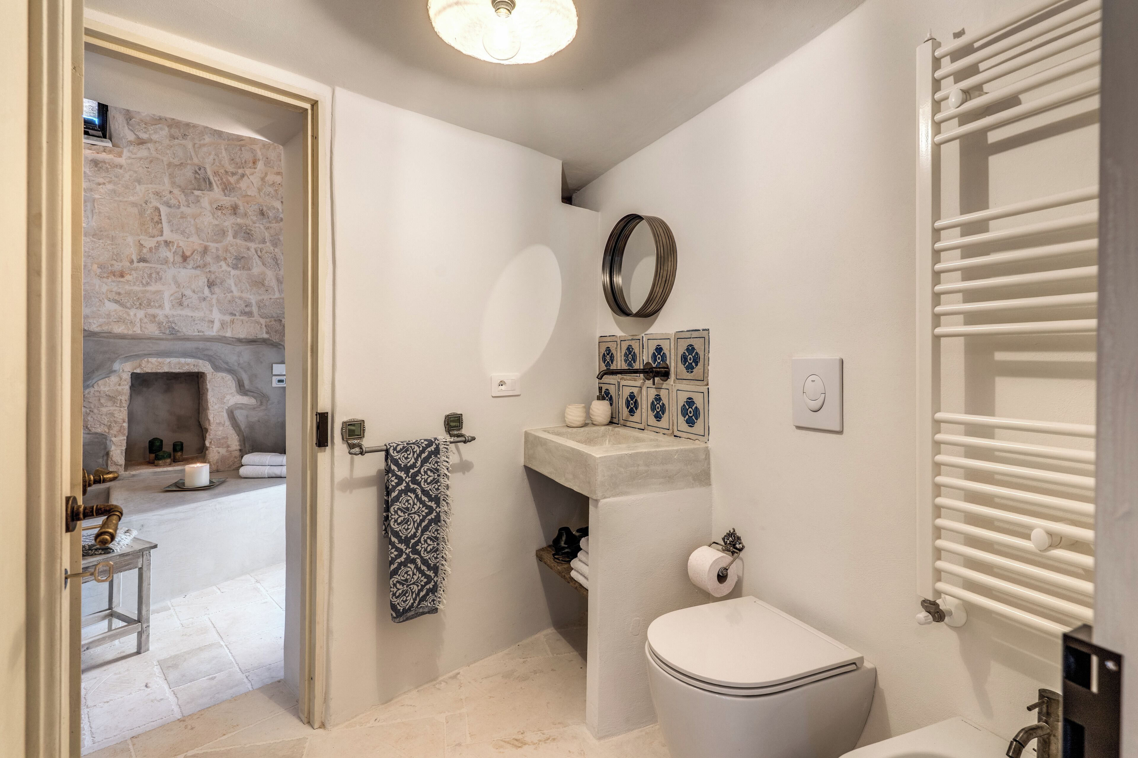A bathroom with a stone wall, a toilet, a sink, a mirror, and a towel rack.