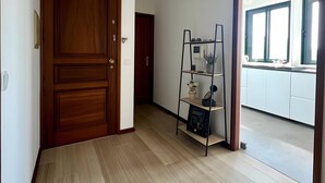 Um corredor com uma porta de madeira, uma estante de metal em escada e um luminária no teto.