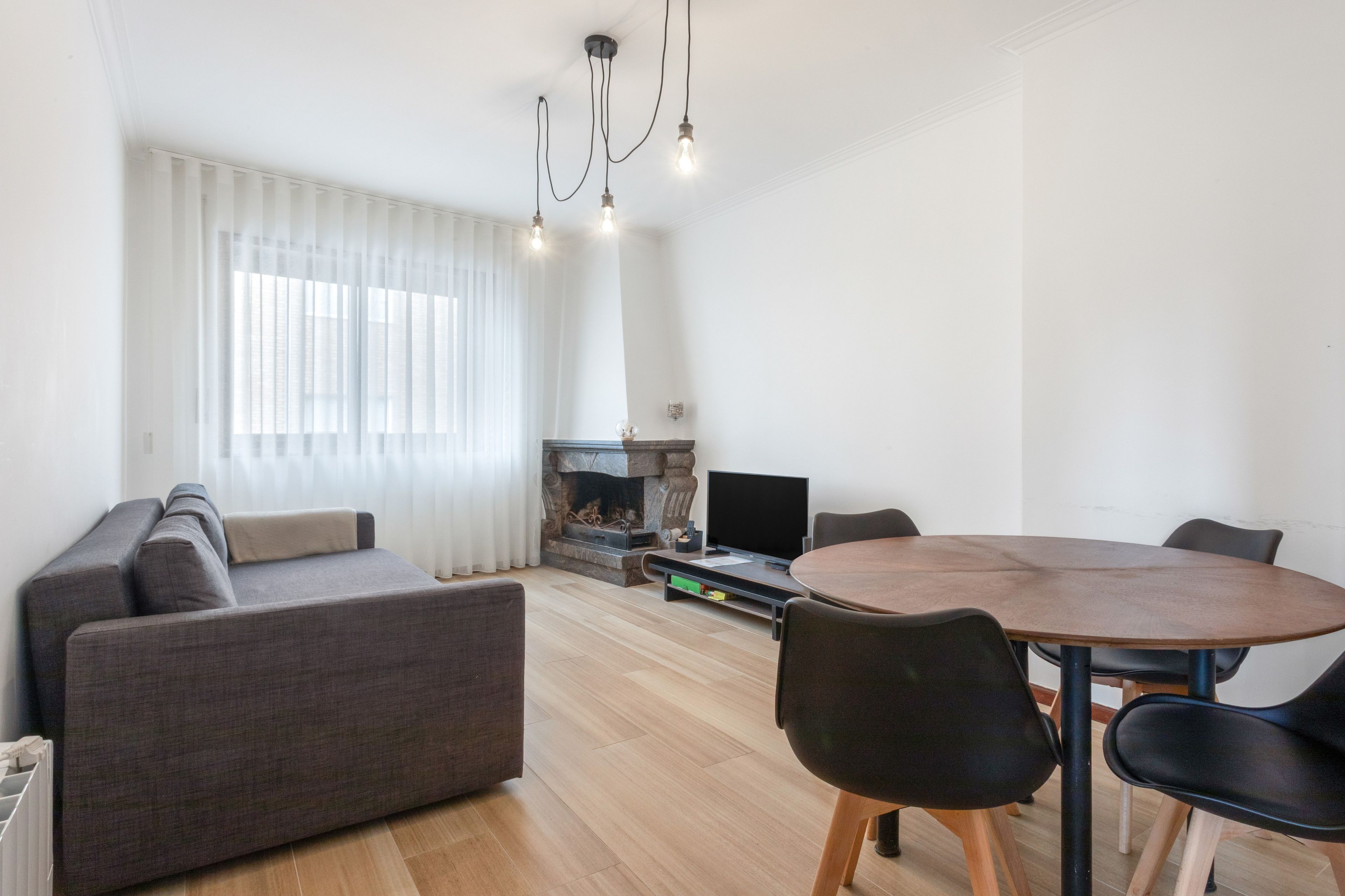 A modern living room with a sofa, a dining table with chairs, a fireplace, and a television.