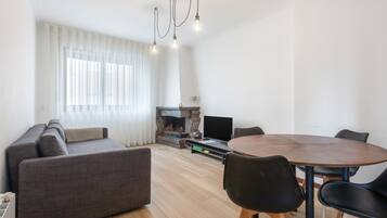 A modern living room with a sofa, a dining table with chairs, a fireplace, and a television.