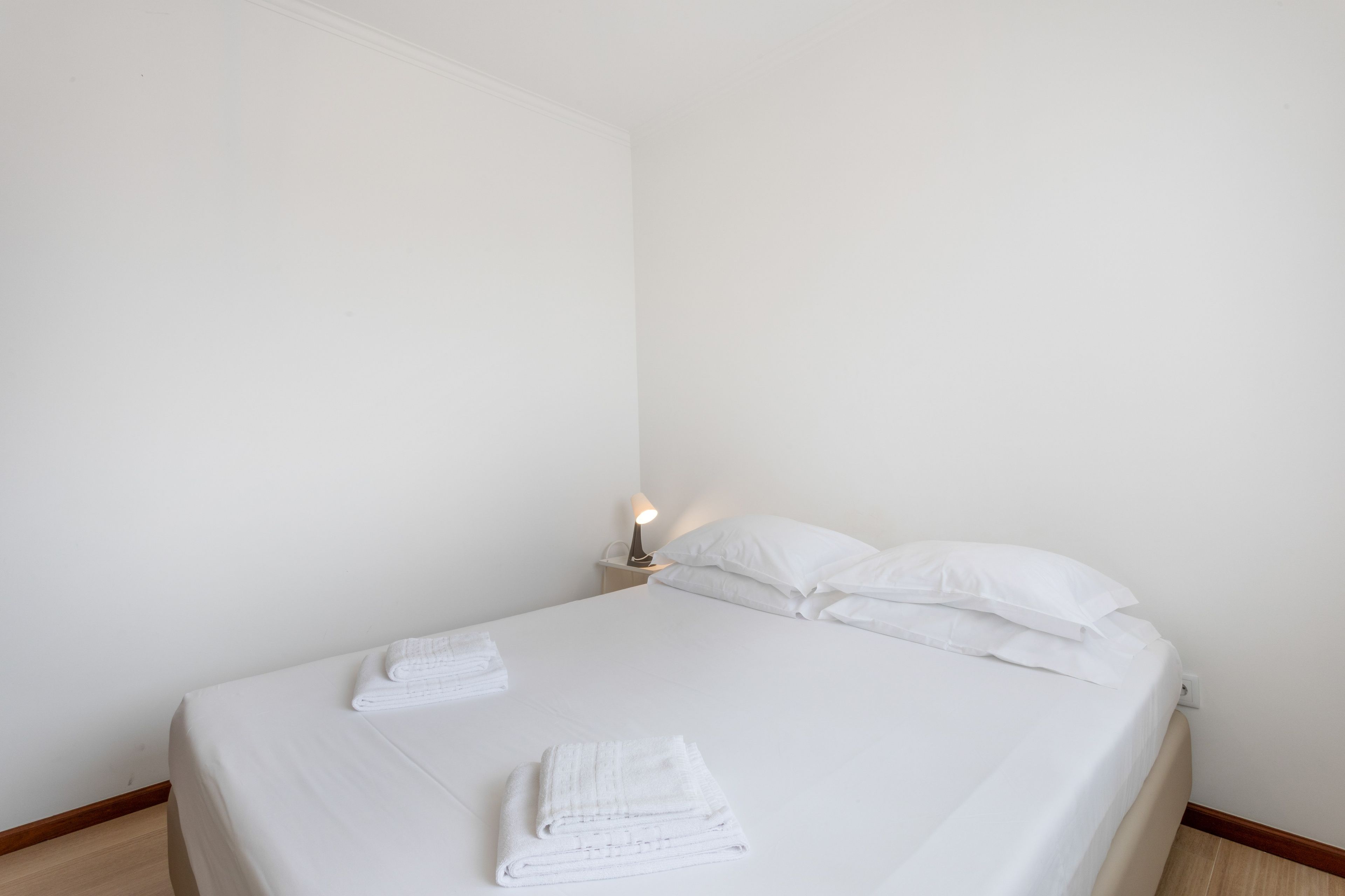 A single bed with white linens, two pillows, and a folded white towel on the bed.