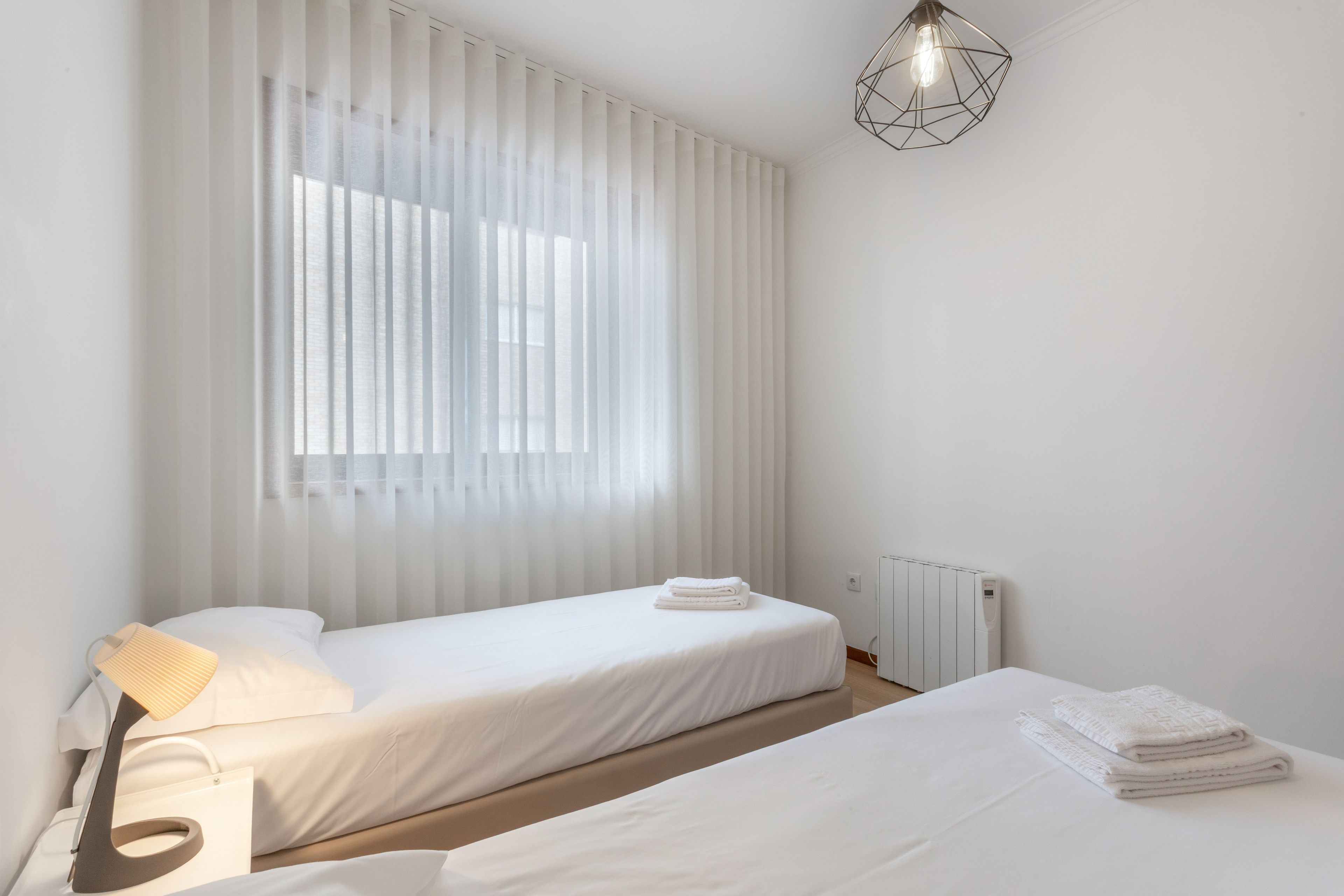 Un dormitorio minimalista con dos camas, un radiador y una lámpara moderna.