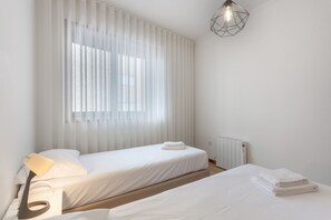 Ett minimalistiskt sovrum med två sängar, ett element och en modern lampa.