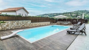 Une piscine bordée d’un muret en pierre et dotée d’une terrasse en bois, entourée de chaises longues et d’un espace salon abrité.