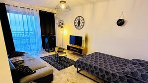 Ein modernes Wohnzimmer mit einer Couch, einem Fernseher, einer dekorativen Uhr und einer hängenden Pflanze.