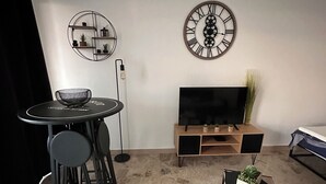 Ein modernes Wohnzimmer mit einem runden Esstisch, einer schwarzen Couch, einem Fernseher auf einem Holzboden und Wanddekoration.