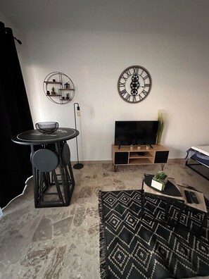 A modern living room with a round dining table, a black sofa, a TV on a wooden stand, and decorative wall art. - Incredible sea view with large terrace and private parking in the center of town (San-Nicolao)