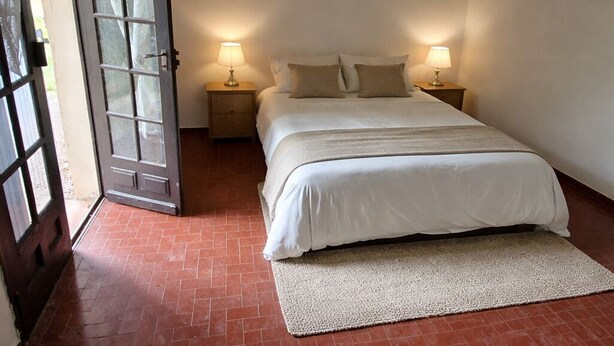Una camera da letto con un letto, due comodini, una porta e un pavimento in piastrelle rosse.