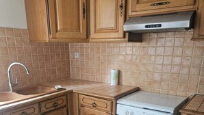Cucina con mobili in legno, lavello in acciaio inox, piano cottura bianco e pavimento piastrellato beige.
