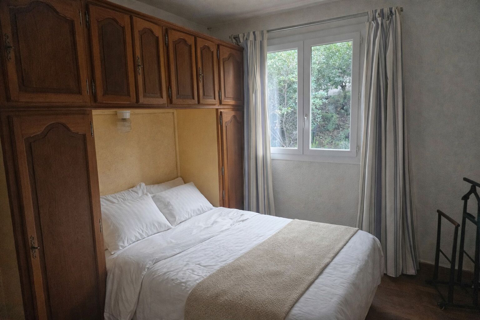 Ein Schlafzimmer mit Bett, Holzschrank und einem fenster mit Vorhängen.