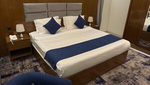 A hotel room with a large bed, a bedside table with a lamp, a chair, and a small round table with a tissue box. - Hayat Al Aseel Hotel Apartments (Jeddah)